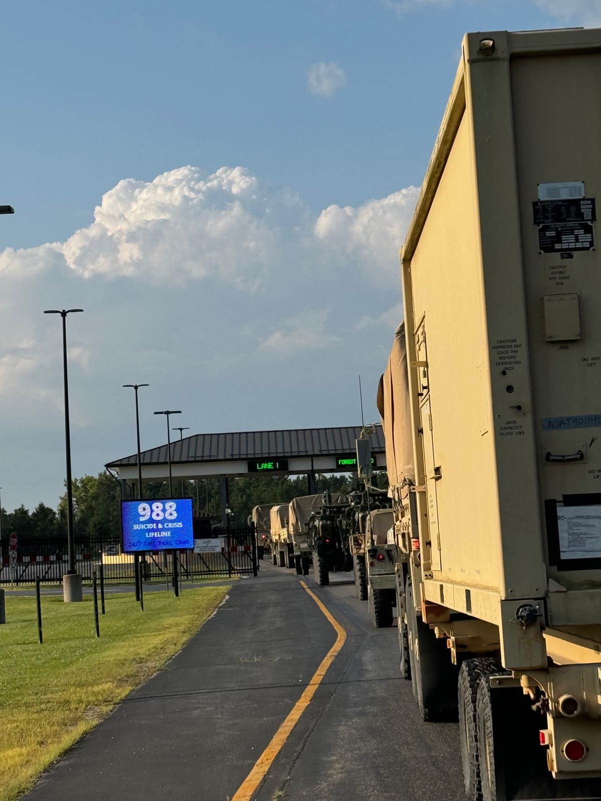 Convoy of vehicles staged at an installation gate at dusk